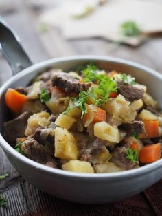 a bowl filled with meat and vegetables on top of a wooden table