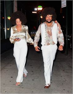 a man and woman dressed in white walking down the street with an afro on their head