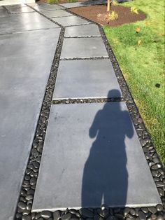 the shadow of a person standing in front of a house on a walkway with stones