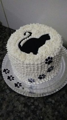 a cake with white frosting and black cat design on the top is sitting on a table