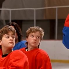 three young boys in red and blue hockey uniforms sitting on the ice with their arms around each other