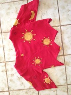 a red shirt with sun and moon designs on it sitting on the floor next to a tiled floor