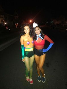 two women in costumes standing next to each other on the street at night with their arms around each other