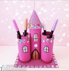 a pink castle made out of toilet paper with makeup brushes and lipstick in it on a table