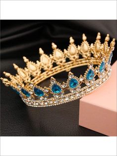 a gold tiara with blue stones and pearls on the side, sitting next to a pink box