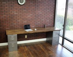 a desk with a laptop on it in front of a brick wall and wooden floor