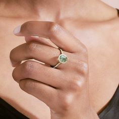 a woman's hand holding a ring with an oval green gemstone on it