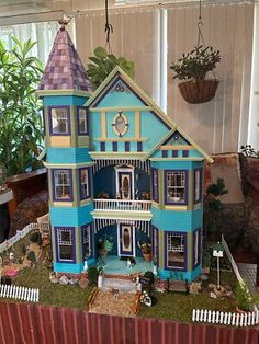 a blue and yellow doll house sitting on top of a wooden table next to a potted plant