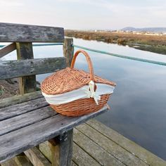 a wicker basket sitting on top of a wooden bench next to a body of water