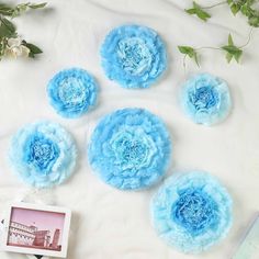 five blue flowers are arranged on a white surface next to a book and some green leaves