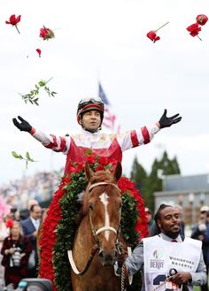 a man riding on the back of a brown horse next to red flowers and greenery