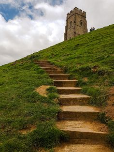 stairs lead up to the top of a grassy hill with a tower in the background