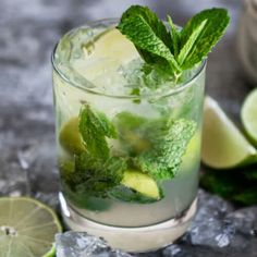 a mojito cocktail with limes and mint on the rocks next to it