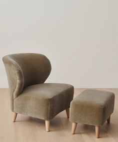 an upholstered chair and footstool on a wooden floor in front of a white wall