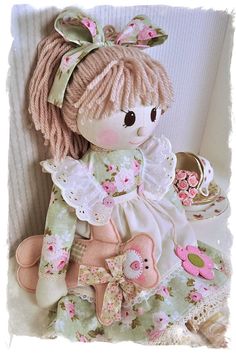 a little doll sitting on top of a bed next to a teddy bear and other items