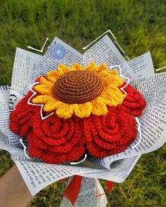 a crocheted sunflower is sitting on top of some folded paper in the grass