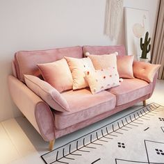 a pink couch with pillows on top of it in front of a white rug and window