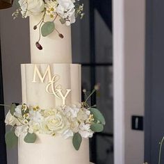 a three tiered wedding cake with white flowers and greenery