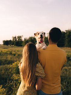 a man and woman holding a small dog in their arms while looking at the sky