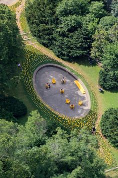 an aerial view of a circular park with yellow benches and flowers on the ground, surrounded by trees