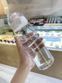 a person holding up a bottle of water in front of a display case at a store