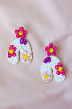 two white and pink crocheted flowered mittens on a pink surface with one hand holding the other