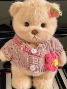 a brown teddy bear wearing a pink sweater sitting on top of a piano with an apple on it's head