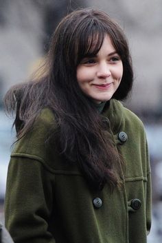 a woman with long hair smiling and wearing a green peal coat on her cell phone