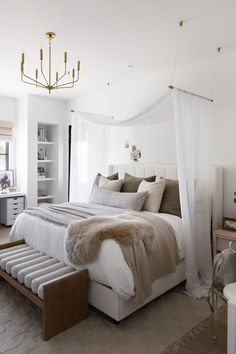 a bedroom with a large bed, white walls and beige carpeted flooring that has a chandelier hanging from the ceiling