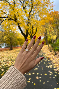 a woman's hand with red nail polish holding onto an orange and yellow tree