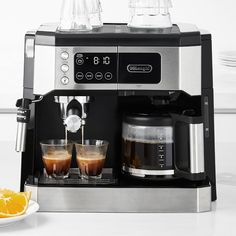 an espresso machine with two cups on the side and orange slices next to it