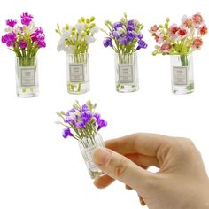 small glass vases with flowers in them being held by a person's hand