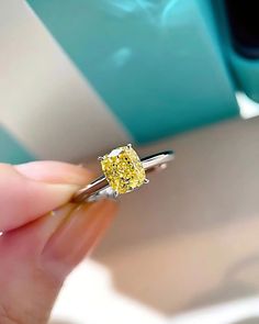 a person holding a yellow diamond ring in their hand