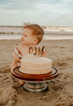 a baby sitting in front of a cake on the beach