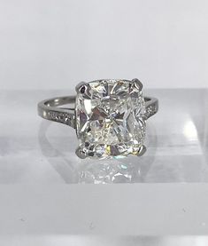 a cushion - cut diamond ring sits on a clear surface