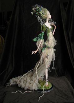 a statue of a woman in white and green dress with flowers on her head, standing against a black background