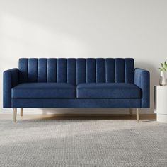 a blue couch sitting on top of a carpeted floor next to a white vase