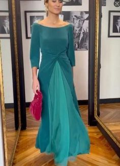 a woman standing in front of a mirror wearing a green dress and holding a pink purse