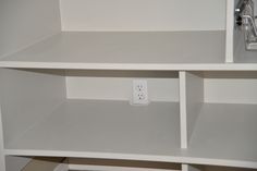 an electrical outlet in the corner of a white bookcase with two shelves on each side