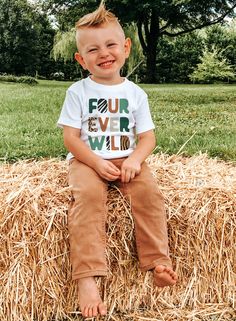 a young boy sitting on top of a pile of hay smiling at the camera with his hands in his pockets