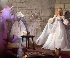 a barbie doll dressed in white standing next to a purple dragon and other figurines