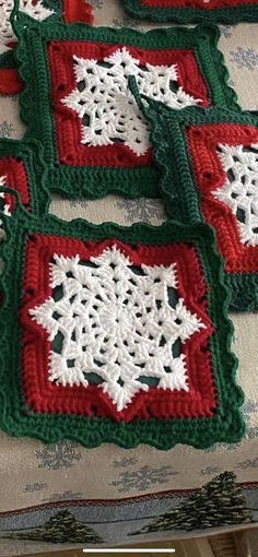 four crocheted squares with red and white designs on them sitting on a table