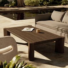 a table sitting on top of a patio next to a couch and coffee table in front of a pool