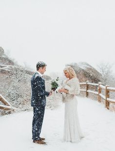 a bride and groom are standing in the snow together, looking at each other as they hold flowers