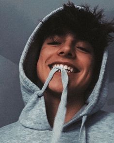 a young man wearing a hoodie and holding a toothbrush in his mouth while smiling