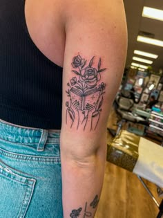 a woman with a tattoo on her arm holding a book and flowers in front of her