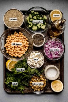 the ingredients for this salad are arranged in separate bowls on a serving tray, including lemons, cucumbers, chickpeas, red onions, parsley, and spinach