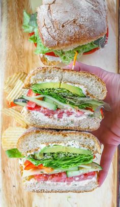 two sandwiches with lettuce, tomato, and cheese are on a cutting board