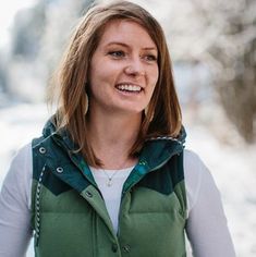 a woman standing in the snow wearing a green vest