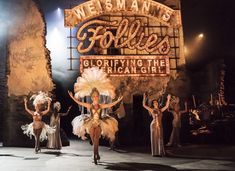 some women are dancing on stage in front of a sign that says follies